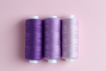 Spools of colorful sewing threads on pink background, flat lay