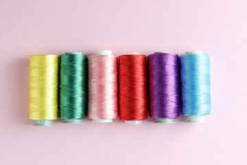 Spools of colorful sewing threads on pink background, flat lay