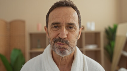 Handsome hispanic mature man in a wellness spa wearing a white robe, looking serene and relaxed...