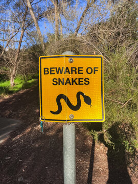 Yellow sign warns of snake danger in wooded trail area in Melbourne