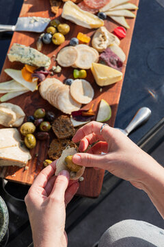 Hands arranging snacks on elegant wooden charcuterie board