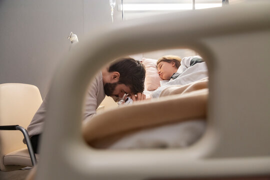 Father praying for sleeping daughter in hospital bed