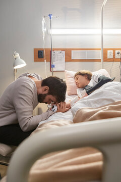 Father praying for his sick daughter in hospital room