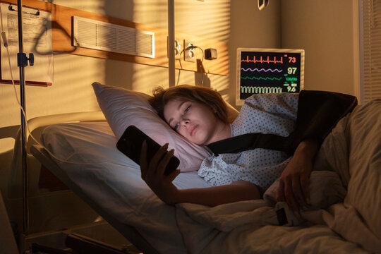 Young patient using smartphone while resting in hospital bed