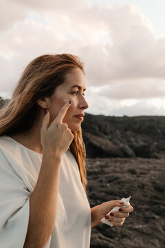 Pregnant woman applying facial cosmetics while posing outdoors