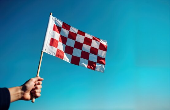 Person holds checkered race flag against bright clear sky. Race competition about to finish. Flag signals winning moment. Sport event in progress. Event could car racing, motor sport, rally.