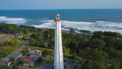 A light house with a black sand beach in the background seen from above