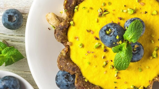 Vegan food dessert. Raw vegan yellow mango cake with fresh blueberries, pistachios and mint. Healthy delicious gluten free food. Top view
