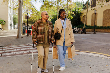 Caregiver walking with elderly woman using crutches on city street