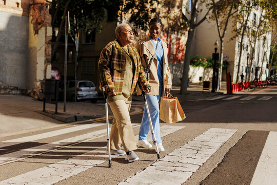 Caregiver helping elderly woman crossing street