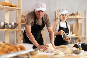 Skilled male baker kneading dough and teenage girl whipping ingredients in metal bowl in bakehouse