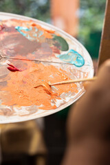 Confident painter mixing different watercolors on a palette to create the perfect dye shade and apply on canvas, working on fine art. Artist uses vibrant colors and dynamic brushwork. Close up.