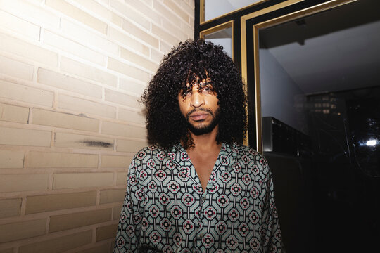 Man in Patterned Shirt Leaning Against Brick Wall