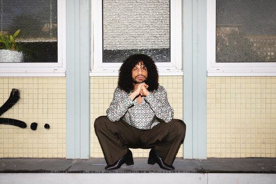 Man Squatting in Front of Tiled Wall