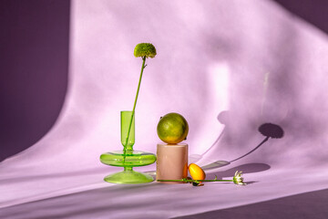 Green vase with fruits and flower on purple backdrop