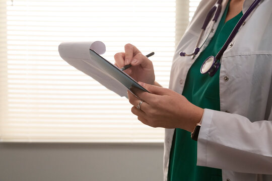 Female doctor writing medical notes on clipboard in hospital room