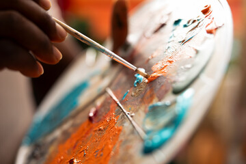 Obraz premium In an art studio, painter mixes multiple watercolor paints on a palette to create a new artwork on canvas. Skilled man painting with tools and showing his imagination, artistic creation. Close up.