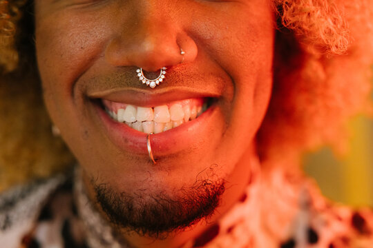 Close-up of smiling lips with facial piercings in warm lighting