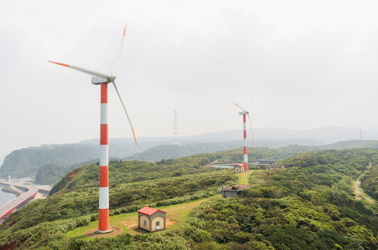 Wind turbines on a lush green hill with small buildings
