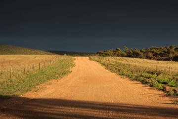 Sunlit gravel road with storm clouds in the distant sky. Australia.