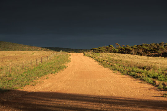 Sunlit gravel road with storm clouds in the distant sky. Australia.