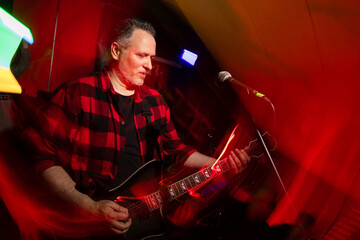 Electric guitarist in plaid shirt performing under colorful lights