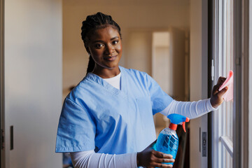 Assistant cleaning window glass with disinfectant spray at apartment