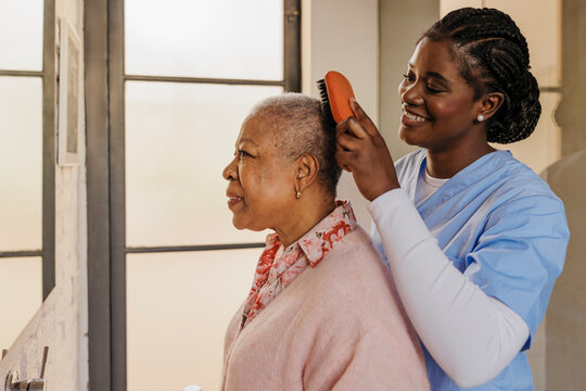 Caregiver brushing hair of elderly woman in bathroom