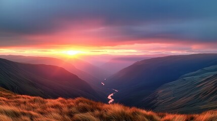 A panoramic view of a mountain sunset, with shadows deepening in the valleys and the sky ablaze with fiery colors.