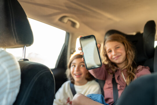 Siblings at the back of the car playing with a phone