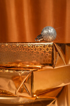 A silver sparkling Xmas bauble on gift boxes wrapped in golden paper. 
