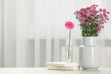 Beautiful pink flowers in vases and books on table at home, space for text