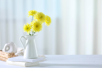 Beautiful yellow flowers in vase and books on white wooden table at home. Space for text