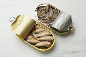 Tasty sprats in tin cans on white marble table, top view