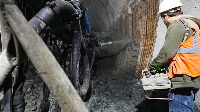 A worker commands concrete spraying on a wall with a remote control