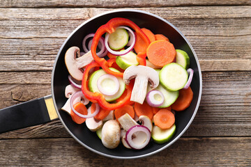 Frying pan with mix of fresh vegetables and mushrooms on wooden table, top view