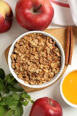 Delicious apple crisp in bowl, fresh fruits, mint, honey and cinnamon stick on white table, flat lay