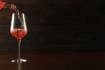 Pouring rose wine into glass at wooden table, space for text