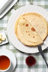 Delicious crepes, tea, butter and jam on table, flat lay
