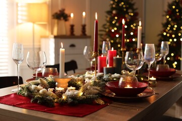 Christmas table setting with stylish dishware, glasses and burning candles in festive decorated room