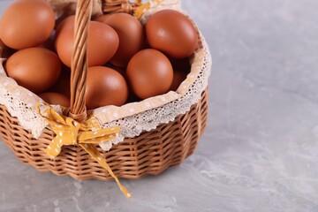 Wicker basket with fresh eggs on grey marble table, closeup. Space for text