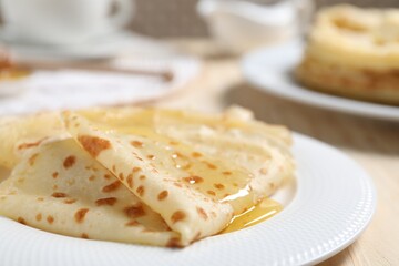 Tasty crepes with honey on wooden table, closeup