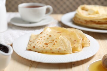 Tasty crepes with honey on wooden table, closeup