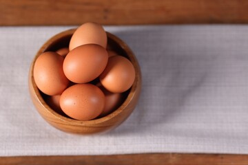Fresh eggs in bowl on wooden table, closeup. Space for text