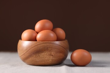 Fresh eggs in bowl on table against brown background, closeup