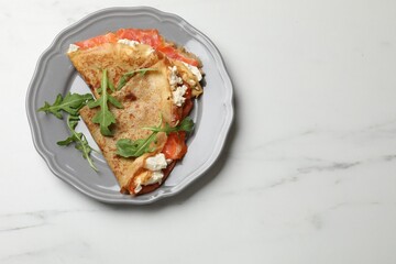 Delicious crepes with salmon, cream cheese and arugula on white marble table, top view. Space for text