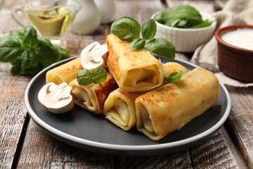 Delicious rolled crepes with mushrooms and basil on wooden table, closeup