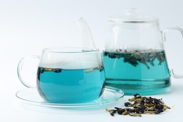 Fresh butterfly pea flower tea in cup, kettle and dry petals on white table, closeup
