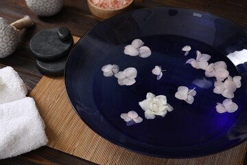 Bowl of water with flowers and different spa supplies on wooden table, closeup