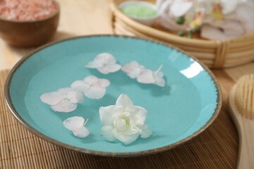 Bowl of water with flowers and different spa supplies on table, closeup